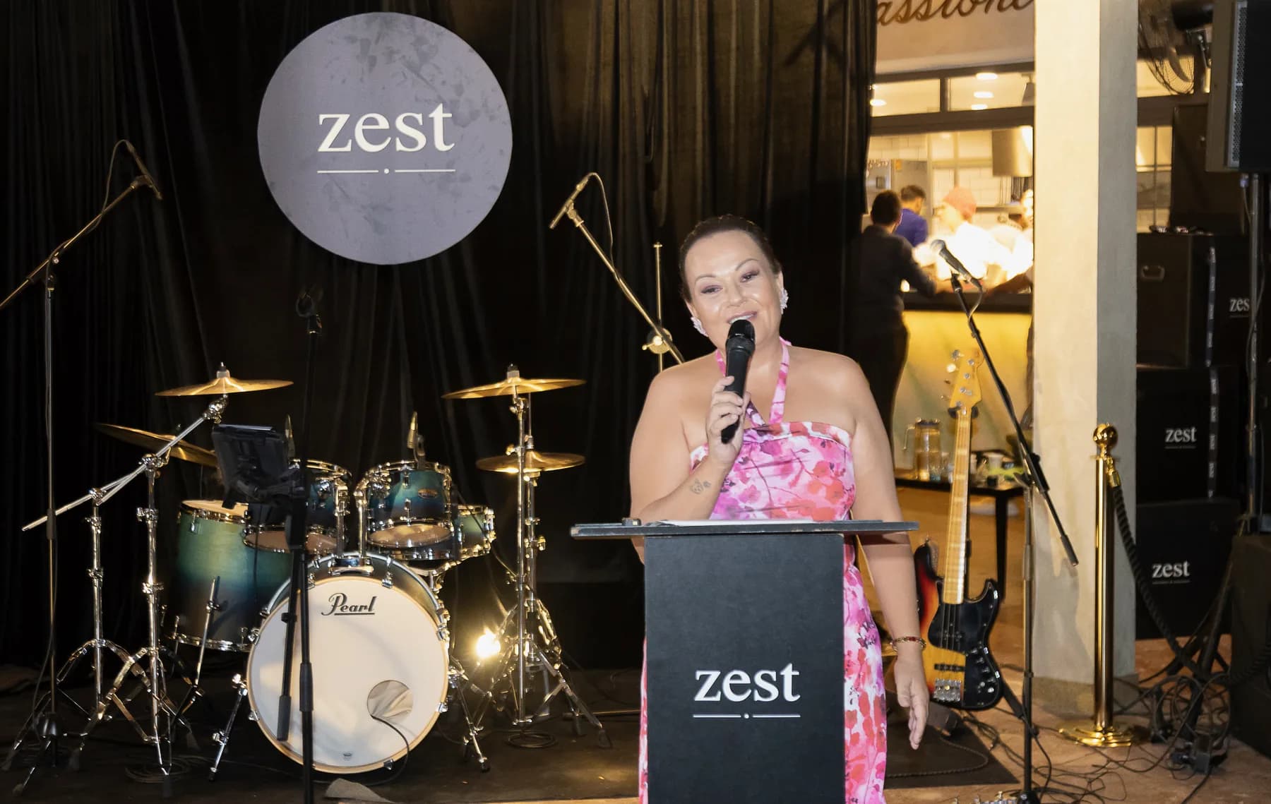 zest lansmanı: Özlem kürsüde mikrofonu ağzına yaklaştırmış konuşuyor, üstte zest logosu.